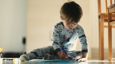 Téléchargez les photos : Créativité tôt le matin - Enfant en pyjama Croquis avec stylo bleu sur le sol - en image libre de droit