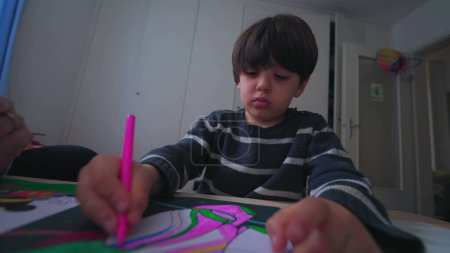Foto de Dibujo infantil concentrado en el dormitorio, niño pequeño con pluma para colorear en papel - Imagen libre de derechos