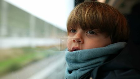 Téléchargez les photos : Enfant pensif voyageant en train penché sur la fenêtre regardant les paysages passer à grande vitesse. un petit garçon caucasien portant écharpe fixe à vue de wagon - en image libre de droit