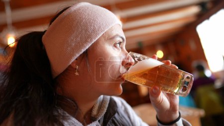 Photo for Woman Savoring Chilled Draft in Cold Season, Profile View of Female Sipping Beer in Restaurant chalet - Royalty Free Image