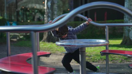 Photo for Child playing at playground carousel during autumn season. Little boy spinning in circles while holding on metal bar getting exercise and outdoor activity - Royalty Free Image