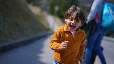Foto de Niño de ojos brillantes en amarillo corriendo alegremente en el escenario de otoño? La expresión animada del niño mientras corre al aire libre en otoño - Imagen libre de derechos