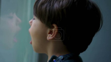 Téléchargez les photos : Enfant respirant de l'air dans le verre de fenêtre créant condensation, moment d'enfance ludique - en image libre de droit