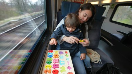 Téléchargez les photos : Mère dévouée et son enfant s'engagent dans une tâche scolaire à bord d'un train à grande vitesse, en utilisant le temps de voyage de manière productive - en image libre de droit