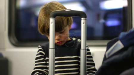 Foto de Pequeño pasajero jugando con el asa superior de la maleta. juego en solitario del niño que pasa el tiempo mientras viaja en tren - Imagen libre de derechos