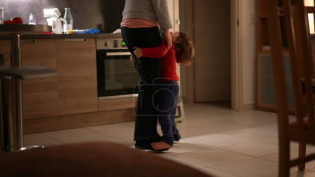Téléchargez les photos : Mère franche jouant avec son petit garçon fils, enfant sur les orteils et les pieds de maman dansant dans le salon de la cuisine - en image libre de droit