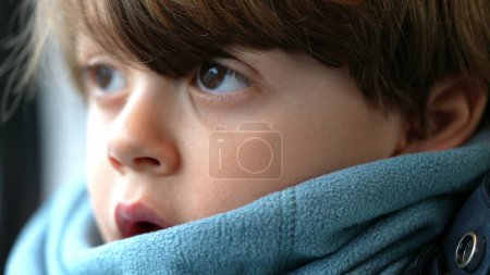 Foto de Cara de niño pensativo de cerca en profunda emoción reflexiva con bufanda. Un pequeño chico caucásico perdido en el pensamiento - Imagen libre de derechos