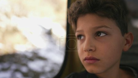Photo for Close-up face of contemplative child traveling by train staring at scenery pass by with a blank expression, thoughtful kid - Royalty Free Image
