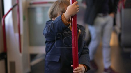 Photo for Child holding into train metal vertical bar turning in circles to pass the time while traveling commute - Royalty Free Image