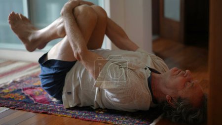Photo for Senior man stretching body in the morning. Eldery caucasian person laid on floor exercising, stretches back. Body health in old age - Royalty Free Image
