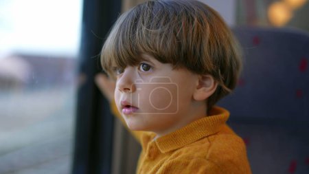 Foto de Cara de niño de cerca mirando fijamente desde la ventana del tren con expresión curiosa. Un pequeño chico caucásico viajando - Imagen libre de derechos