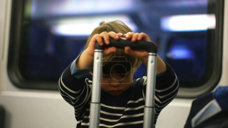 Téléchargez les photos : Enfant seul se distrayant avec une valise en train, petit garçon jouant avec la poignée pendant le trajet - en image libre de droit