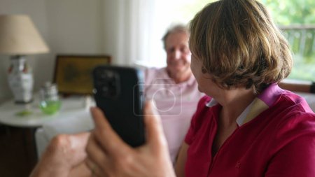 Photo for Senior woman holding smartphone device speaking with family member using video communication to speak in long-distance. Grandparents speaking with relatives - Royalty Free Image