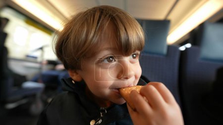 Téléchargez les photos : Gros plan sur le visage d'un enfant heureux qui mange des biscuits au beurre pendant son trajet, biscuit de collation pour petit garçon - en image libre de droit