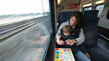 Photo for Attentive mom and son delving into an educational exercise while on a rapid train journey, making the most of their transit time - Royalty Free Image
