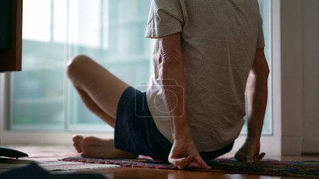 Foto de Hombre mayor levantándose del suelo durante la rutina de ejercicios matutinos. anciano caucásico sentado en posición de loto preparándose para meditar - Imagen libre de derechos