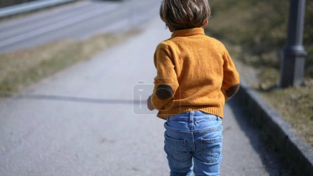Photo for Back of excited small boy sprinting outside during autumn day, Child wearing yellow pullover, jeans, and boots runs - Royalty Free Image