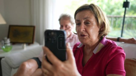 Téléchargez les photos : Femme âgée tenant un téléphone intelligent parlant avec un membre de la famille en utilisant la communication vidéo pour parler à longue distance. Grands-parents parlant avec des parents - en image libre de droit