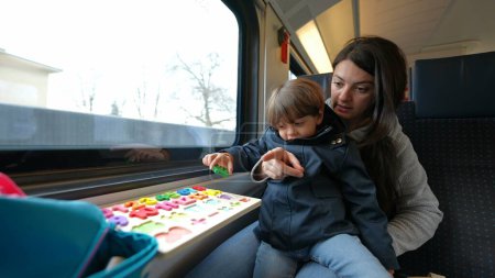 Téléchargez les photos : Mère engagée conduisant une session d'apprentissage avec son enfant à bord d'un train à grande vitesse, illustrant l'éducation mobile de l'enfance - en image libre de droit