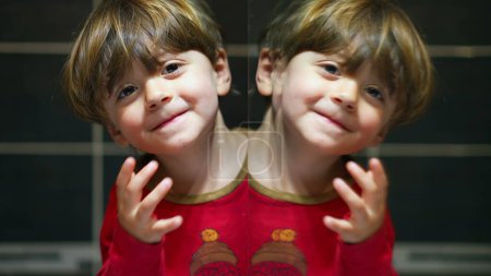 Photo for Humorous child creates twin image in mirror, joyfully peers at camera next to his mirrored self with happy expression - Royalty Free Image