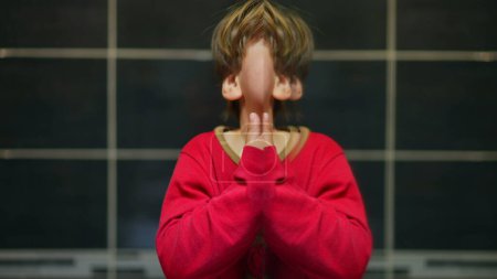 Téléchargez les photos : Enfant humoristique crée une image jumelle dans le miroir, joyeusement pairs à la caméra à côté de son moi miroir avec une expression heureuse - en image libre de droit