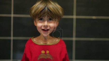 Photo for Playful boy twins his face using bathroom mirror, close-up of cheerful child gazing and playing at camera while leaning on his reflection - Royalty Free Image