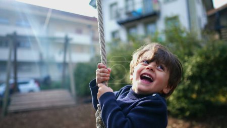 Téléchargez les photos : Enfant excité en gros plan, saisissant et glissant sur un câble métallique entre les arbres - en image libre de droit