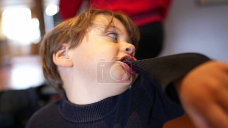 Photo for Idle Antics - Little Boy Biting Sleeve, Expressing Boredom While Waiting at Restaurant - Royalty Free Image