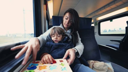 Photo for Mom homeschooling son while on train travel. Child doing school activity with parent while commuting - Royalty Free Image