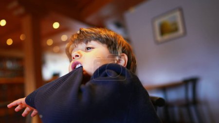 Photo for Boredom Bites, Small Boy Pulling Sleeve with Teeth, Idle at Restaurant - Royalty Free Image