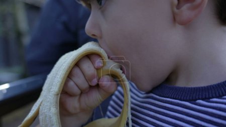Photo for Close-Up of Small Boy Enjoying a Banana, Healthy Snack While Riding a Miniature Train at Railroad Park - Royalty Free Image