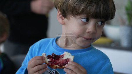 Photo for Child eating brioche bread with jelly for breakfast. Close-up of little caucasian boy eating food in the morning, candid lifestyle scene - Royalty Free Image