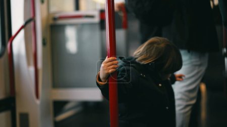 Photo for Whimsical Little traveler on a train, clutching a metal support bar and twirling around it. A snapshot of childhood joy, making the best of the commute with innocent play - Royalty Free Image