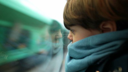 Photo for Little boy leaning on train window looking at landscape pass by at high-speed. Child wearing scarf staring at view in motion - Royalty Free Image