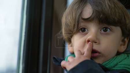 Close-up face of small boy nose picking. Introspective kid traveling by train