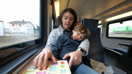 Téléchargez les photos : Mère faisant de l'activité scolaire avec son fils tout en voyageant en train à grande vitesse, concept d'éducation de l'enfance sur la route - en image libre de droit