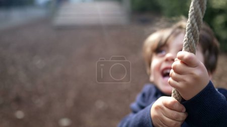 Téléchargez les photos : Joyeux enfant glissant sur la corde à Autumn Playground. Joyeux enfant tenant la corde et profitant de la glissière dans le parc d'automne - en image libre de droit