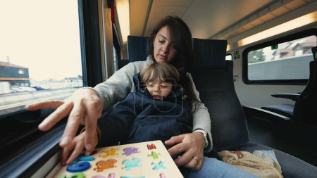 Téléchargez les photos : Mère et enfant voyageant en train à grande vitesse et faisant des activités scolaires pour passer le temps - en image libre de droit