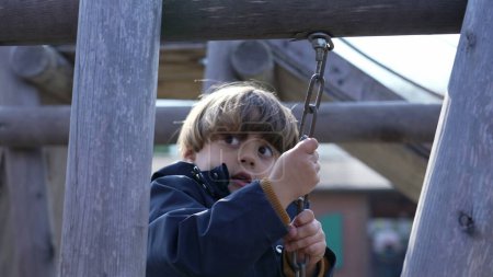 Foto de Niño enfocado navegando por el puente del patio de recreo, sosteniendo cadenas metálicas y pisando tablones de madera - Imagen libre de derechos