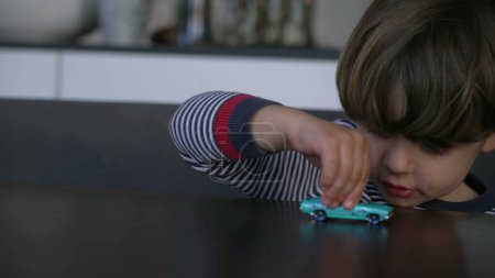 Foto de Primer plano niño jugando coche de juguete. Un pequeño niño caucásico sosteniendo el objeto del vehículo sobre la mesa - Imagen libre de derechos