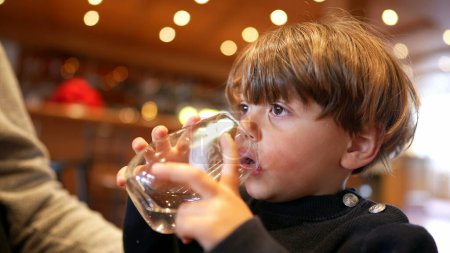 Photo for Little boy sipping water at restaurant. Child drinking and hydrating himself holding glass - Royalty Free Image