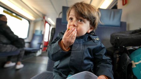 Téléchargez les photos : Jeune voyageur saisissant un récipient de baies, profitant d'une bouchée de fruit nutritive, assis sur un train en mouvement, grignotage en cours de route - en image libre de droit