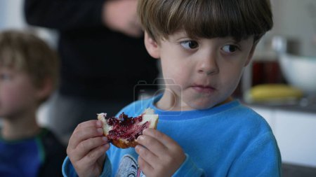 Foto de Niño comiendo pan brioche con gelatina para el desayuno. Primer plano de niño caucásico comiendo comida en la mañana, escena de estilo de vida franca - Imagen libre de derechos