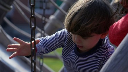 Photo for Child takes hold of chain at playground structure, losing equilibrium, learning to play. Small boy at public park - Royalty Free Image