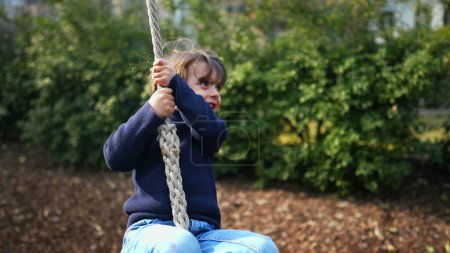 Téléchargez les photos : Jeune garçon saisissant la corde glissante entre les arbres le jour de l'automne, l'enfant s'engage avec enthousiasme dans la glissade de corde au milieu de la saison d'automne - en image libre de droit