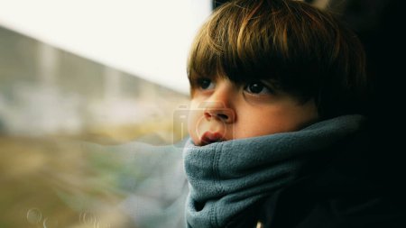 Photo for Thoughtful child staring at landscape pass seated by train window leaning on window wearing scarf. Pensive emotion of kid - Royalty Free Image