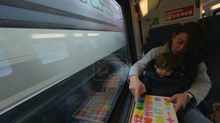 Foto de Mamá proactiva facilitando una actividad educativa para su hijo durante un viaje en tren rápido, ejemplificando el aprendizaje infantil en movimiento - Imagen libre de derechos