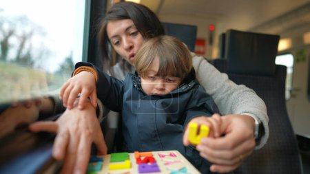 Photo for Young boy settled on mother's lap during train journey, engaging in homeschooling tasks while commuting, epitomizing mobile learning - Royalty Free Image