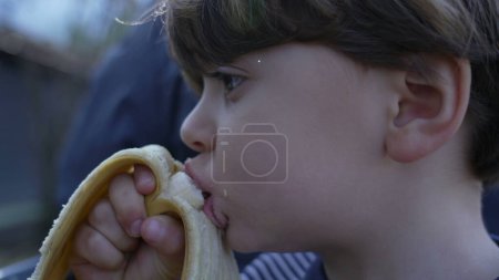 Foto de Primer plano de niño pequeño disfrutando de un plátano, bocadillo saludable mientras monta un tren en miniatura en Railroad Park - Imagen libre de derechos