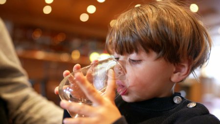 Foto de Un niño bebiendo agua en el restaurante. Niño bebiendo e hidratándose sosteniendo el vaso - Imagen libre de derechos